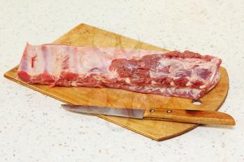 Raw pork ribs and knife on wooden cutting board taken closeup.