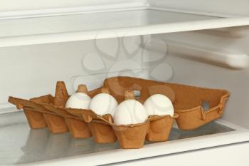 Eggs in a paper box on refrigerator shelf taken closeup.