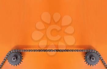 Black metal cogwheels and chain on orange background with empty space for text.