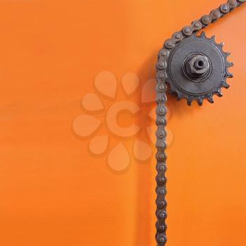 Metal cogwheel and chain on orange background with empty space for text.