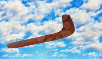 Wooden australian boomerang in flight against of pure white clouds and blue sky.