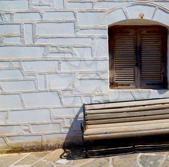 and stone pavement in the greece island of paros old bench near a brick antique wall 