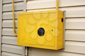 Yellow metal box with a gas device inside hanging outdoors on the wall of a residential building covered with siding