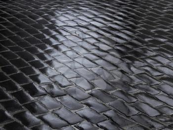 Fragment of wet road covered with dark cobblestone after the rain