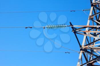 Insulators, wires, and fragment of metal electrical tower on the background of blue sky