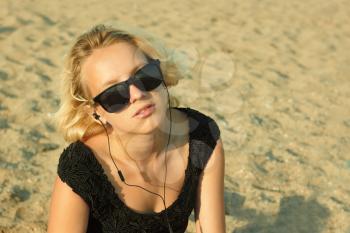 Beautiful teenage blond girl with glasses and headphones on the background of a sandy beach