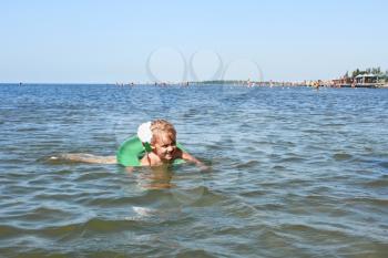 Little girl swimming on inflatable wheel against crowded beach