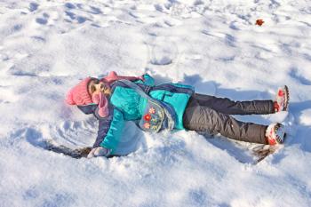 Beautiful little girl on the back lying in a shallow snow in a sunny winter weather