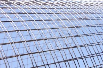Metal grid of white alloy shines in bright sunlight on the blue sky background