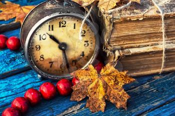 Obsolete alarm clock on background of old books and yellow maple leaf.Photo tinted.