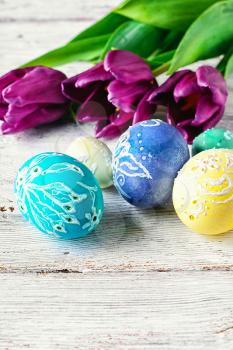 Decorated with painted Easter eggs and bouquet of tulips on light background