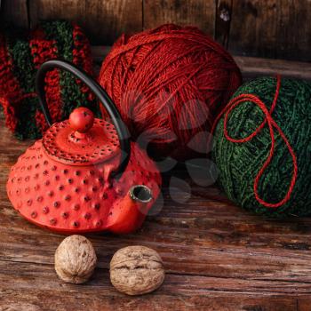 Stylish teapot with warm tea and balls of wool to knit