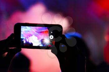Shooting on smartphone festival concert. Blurred music stage bokeh background for design. Fans takes picture of scene on phone