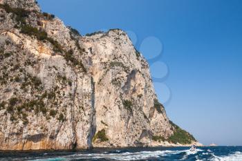 Small touristic motorboat goes near coastal rocks of Capri island, Italy