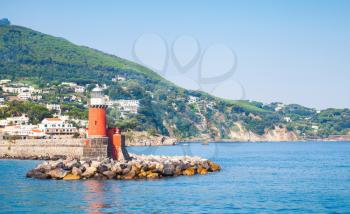 Red lighthouse tower on stone breakwater. Entrance to Ischia Porto. Mediterranean sea, Italy
