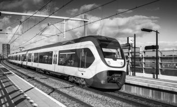 Passenger electric train goes near railway platform in Amsterdam, Netherlands. Black and white photo