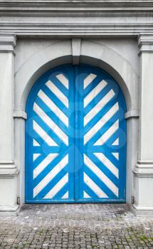 Old wooden door with white and blue stripes pattern in gray stone wall, background texture. Luzern, Switzerland