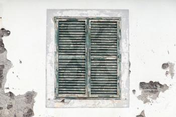 Old window with closed jalousie in white weathered wall, background texture