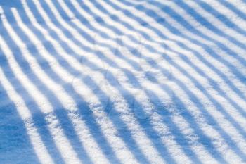Natural background with abstract striped shadow pattern over a snowdrift