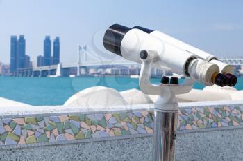 Binocular telescope on a rotating base mounted on an outdoor touristic viewpoint with blurred Busan city landscape on a background. republic of Korea