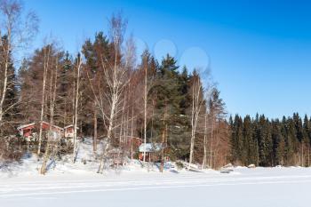 Rural landscape with red wooden houses in coastal forest, Finland in winter