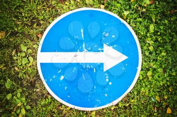 Right only, round blue road sign with white directional arrow lays on green grass