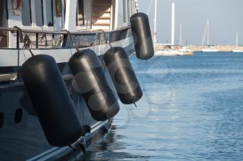 Black rubber inflatable ship fenders hanging above sailing yacht hull