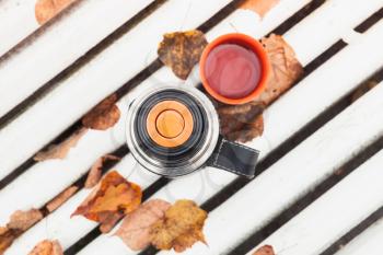 Tourist thermos with cup stands on white bench in autumn park, top view