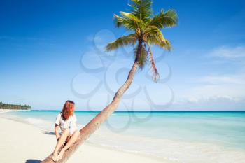 Girl sitting on a palm tree. Saona island beach. Atlantic ocean coast, Dominican Republic