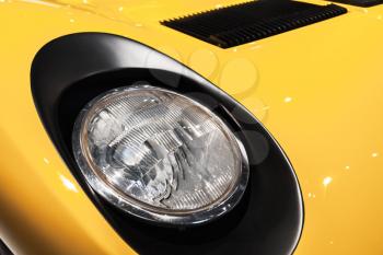 Yellow luxury Italian vintage sport car headlight, closeup photo with selective focus