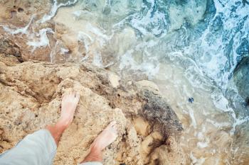 Male bare feet stand on coastal rocks. Travel lifestyle background