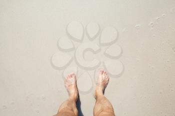 Wet male feet stand on white coastal sand, top view photo