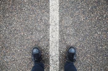 Male feet in blue jeans and black leather shoes stand on street asphalt pavement with dividing line