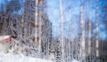 Window frost. Ice crystals pattern on frozen glass with blurred rural landscape background