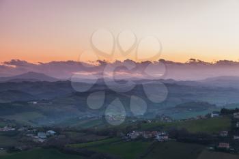 Early morning in Italian countryside. Province of Fermo, Italy. Villages and fields on hills under colorful sky