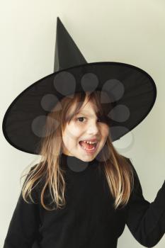 Blond European girl in black witch costume over white wall, close-up studio portrait