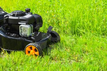 Grass mower stands on fresh green lawn in summer garden