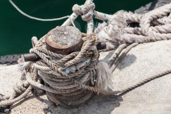 Old rusted mooring bollard with naval ropes stands on concrete pier in harbor