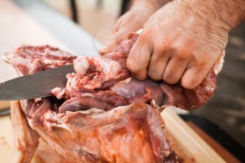 Raw lamb cutting, cook hands with knife, close-up photo, selective focus