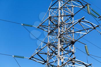 Lattice-type steel tower fragment over blue sky as a part of high-voltage line. Overhead power line details
