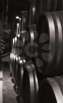 Wooden barrels in dark winery, close up monochrome  vertical photo with selective focus