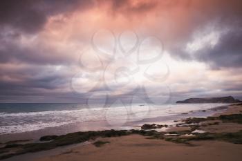 Wet coastal stones with seaweed under dramatic cloudy sky on the beach of Porto Santo island, Madeira archipelago, Portugal