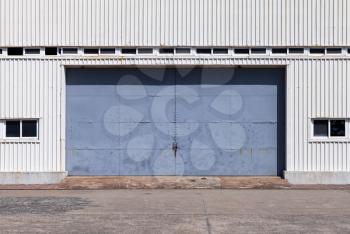 Closed blue gate in white ridged metal warehouse wall, flat background photo texture