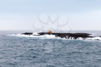 Red navigation mark on small rocky island in Atlantic ocean, Iceland