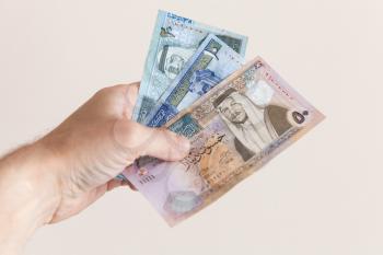 Male hand holding Jordanian dinars banknotes over white wall background