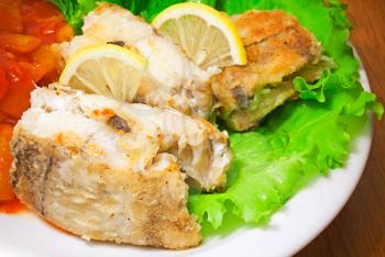 Fried haddock fish with vegetables and greens on white plate, closeup photo