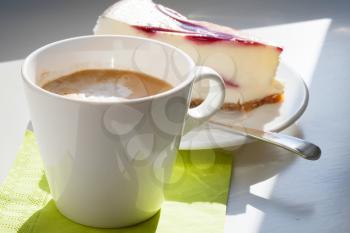 Cup of cappuccino coffee and cheesecake piece on white table. Selective focus
