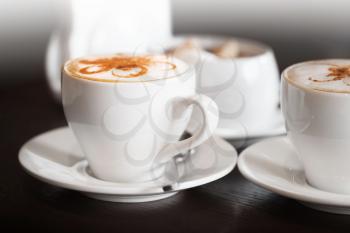 White cups of cappuccino stands on dark wooden table