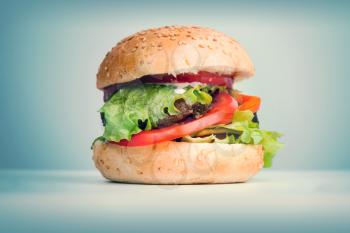 Big hamburger lays on the table above blue background, retro toned photo