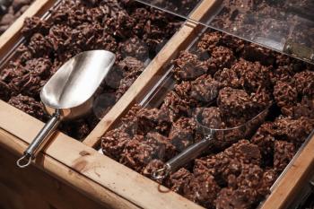 Chocolate with nuts lay on wooden store shelves with metal scoop